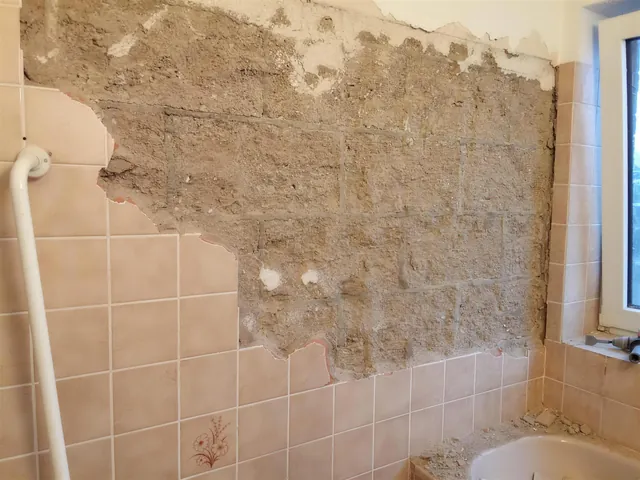Badezimmer während der Entkernung: Fliesen zur Hälfte abgeschlagen, Wand auf Putz zurück.
