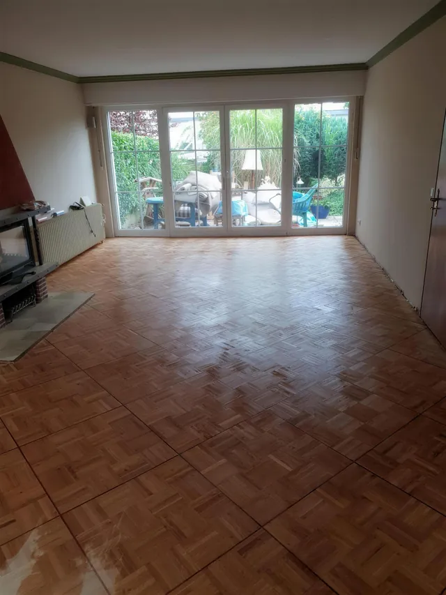 Leergeräumtes Wohnzimmer mit Parkettboden und Blick in den Garten.