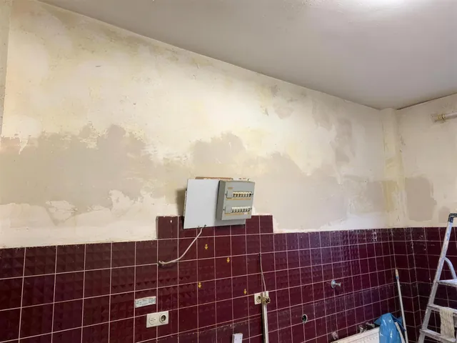 Wand während der Renovierung, alte Tapete und Fliesenspiegel zur Hälfte entfernt.